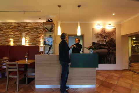 Un espace d'accueil dans un hôtel avec un employé amical et un client. L'atmosphère est chaleureuse et accueillante, avec des couleurs chaudes et un mobilier moderne.