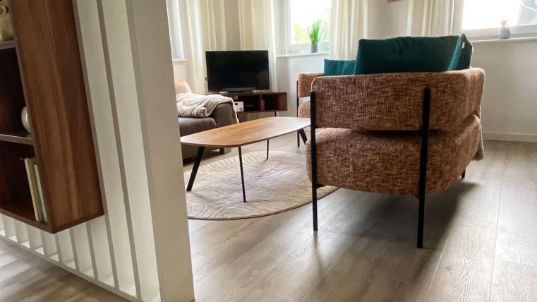 Un salon moderne avec un fauteuil confortable et une table basse en bois. De grandes fenêtres laissent entrer beaucoup de lumière naturelle et créent une atmosphère agréable.