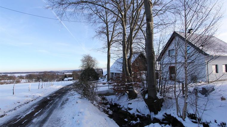 A snowy landscape with a quiet path and several houses. In the background, snow-covered fields and trees can be seen.