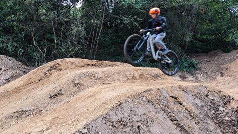 Ein Radfahrer springt mit seinem Mountainbike über einen Hügel im Wald. Der Fahrer trägt einen Helm und sportliche Kleidung.