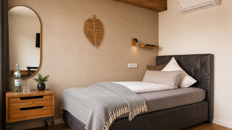 Een moderne slaapkamer met een comfortabel bed, een warme deken en een spiegel aan de muur. De ruimte heeft een ontspannen sfeer met natuurlijke elementen en warme houttonen.