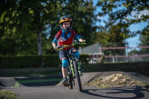 A boy rides a bicycle in a park. He is wearing a helmet and protective gear as he crosses a path.