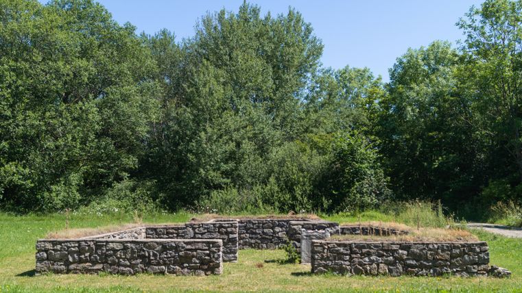 Ruinen eines römischen Tempels auf einer Wiese, umgeben von Bäumen.