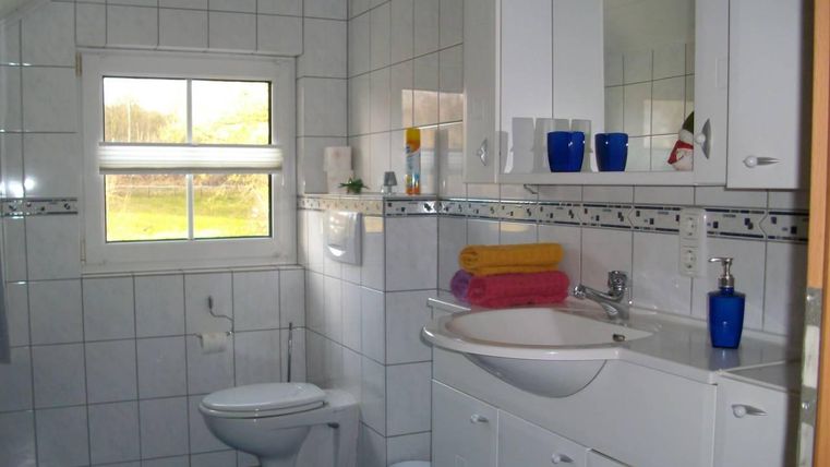 Een moderne badkamer met witte tegels en een groot raam. Op de wastafel liggen kleurrijke handdoeken en er zijn verschillende verzorgingsproducten.