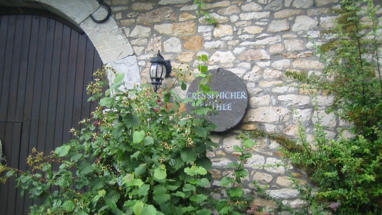A historic stone building with a wooden door and a striking wall lamp. Above the entrance hangs a sign with the inscription "Cress-picher Mill".