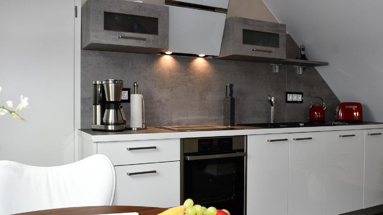 Modern kitchen with bright cabinets and high-quality appliances. On the table, there is a bowl of fresh fruit.