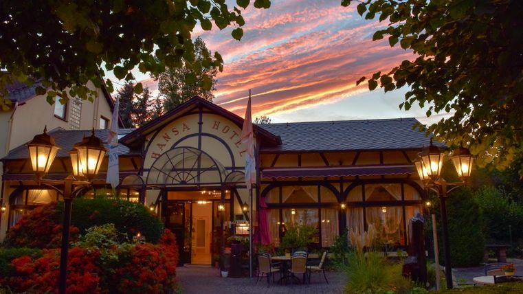 A charming hotel with an inviting, historical facade and romantic lanterns. The sky is colored in warm hues during sunset.