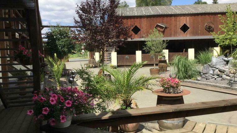 Une magnifique cour intérieure avec des plantes et des fleurs colorées. En arrière-plan, on peut voir des bâtiments en bois et une petite installation d'eau.