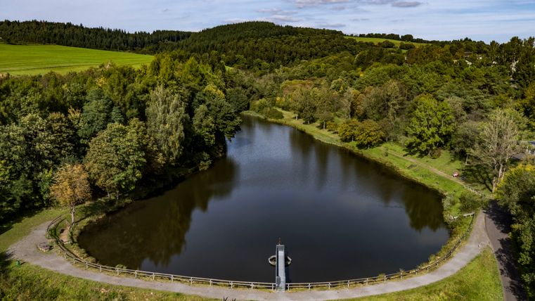 Vue d'en haut sur le lac de barrage de Gerolstein, entouré de forêts et de prairies. Le lac bleu foncé se détache de la nature verdoyante.
