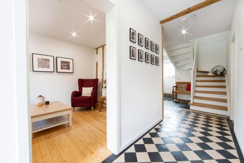 Een lichte gang met een schaken vloerbedekking en een trap. Aan de linkerkant staat een rode fauteuil en hangen er enkele schilderijen aan de muur.