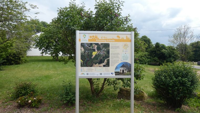 Informatiebord over de kruisweg in Sefferweich, omgeven door bomen en struiken.