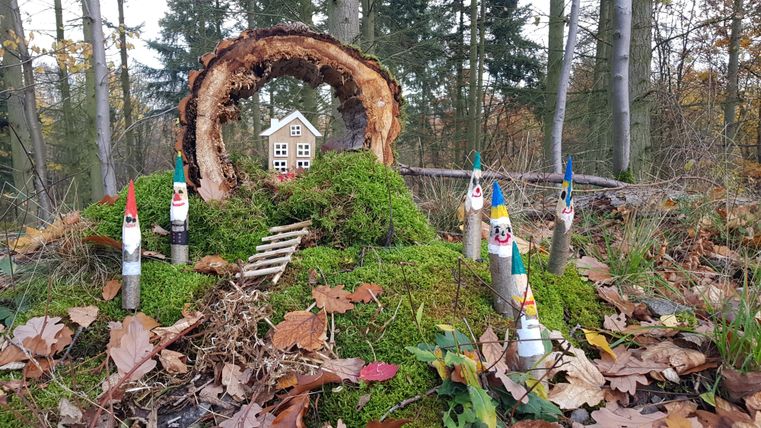 Eine kleine, fantasievolle Szene im Wald mit einem Häuschen und bunten Figuren aus Holz. Umgeben von Moos und Herbstblättern.