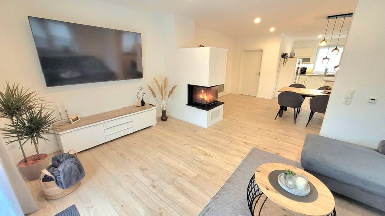 A modern living room with a large television and an elegant fireplace. The room is bright and inviting, with stylish furniture and a natural ambiance.