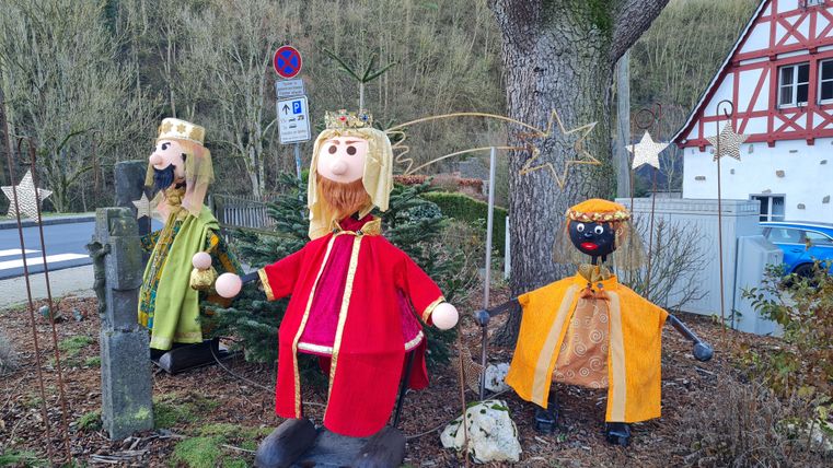 Drei Figuren der Heiligen Drei Könige in bunten Gewändern stehen im Freien vor einem Baum.