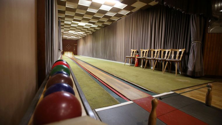 Een bowlingbaan met meerdere kleurrijke kegels en een lange baan. Aan de zijkant staan houten stoelen tegen een muur.