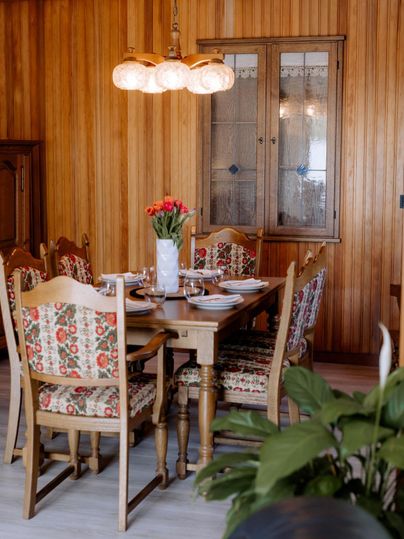 An inviting dining area with a wooden table and colorful chairs. On the table sits a vase with flowers and the dishes are set for the meal.