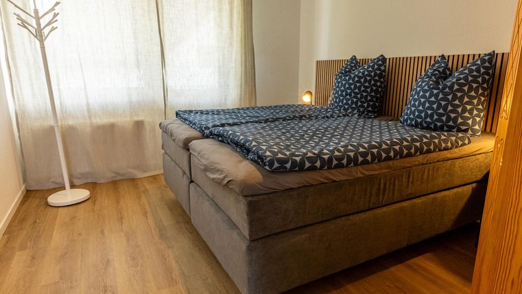Een gezellige slaapkamer met een groot tweepersoonsbed en kleurrijke kussens. De helderheid van de kamer wordt versterkt door de gordijnen en het raam.