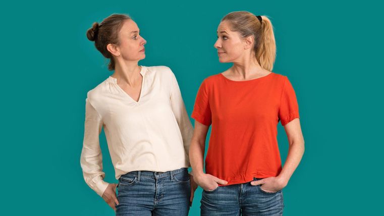 Zwei Frauen stehen nebeneinander und schauen sich an. Die eine trägt ein weißes Hemd, die andere ein rotes T-Shirt.