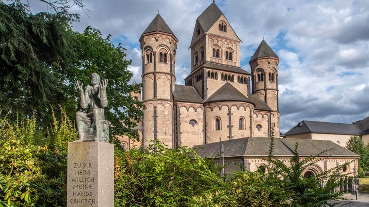 Eine beeindruckende Kirche mit markanten Türmen und einem historischen Steinbau. Im Vordergrund steht eine Statue, die Aufmerksamkeit auf die Umgebung lenkt.