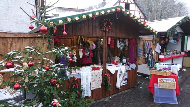 A festive Christmas market stall with lights and decorations. Surrounded by Christmas trees and snow, it offers handmade items and treats.