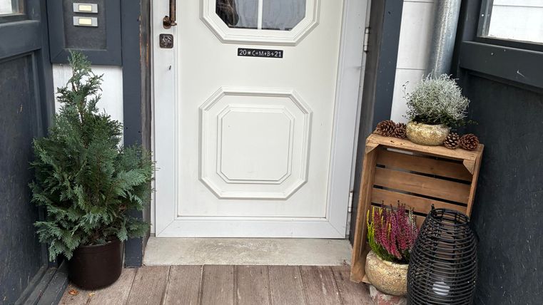 Een uitnodigende voordeur met een gezellige deurmat en een decoratie van planten. De tekst "Wat fijn dat je er bent" straalt een hartelijke welkom uit.