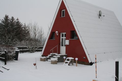 A red house in A-frame style, surrounded by fresh snow. The landscape is wintry and peaceful.