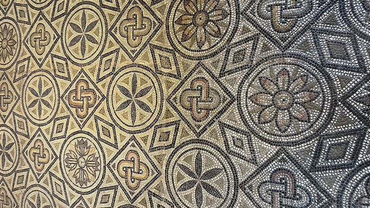 Een elegante mozaïekvloer met verschillende geometrische patronen en florale motieven. De kleuren zijn in neutrale tinten gehouden, wat het ontwerp een klassieke uitstraling geeft.