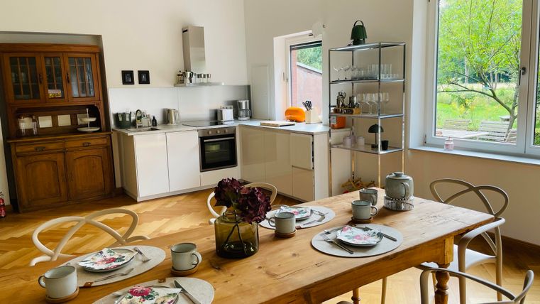 Une cuisine lumineuse avec une table en bois et des meubles modernes. La table est soigneusement dressée avec de la vaisselle et des fleurs.