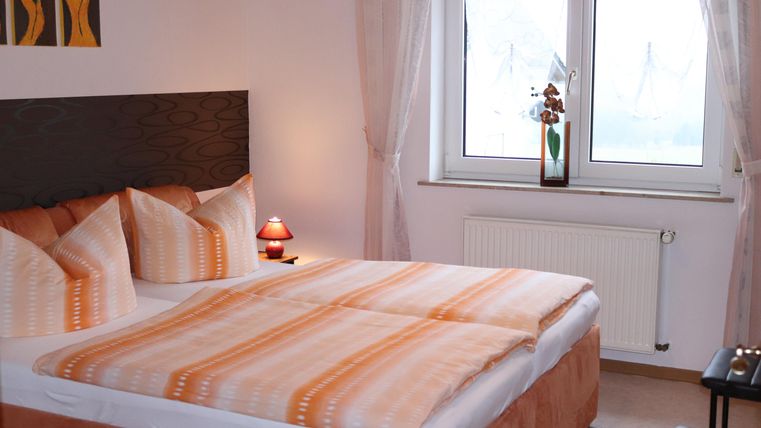 A stylish bedroom with a large double bed and orange bedspreads. Bright windows create a friendly atmosphere and a pleasant decor.