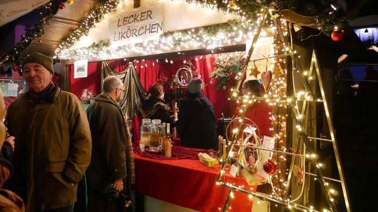 A festively decorated Christmas stall with lights and red fabric. People are buying treats and enjoying the wintry atmosphere.