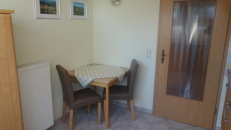A small dining area with a table and two chairs. On the wall are pictures and a door leads to another room.