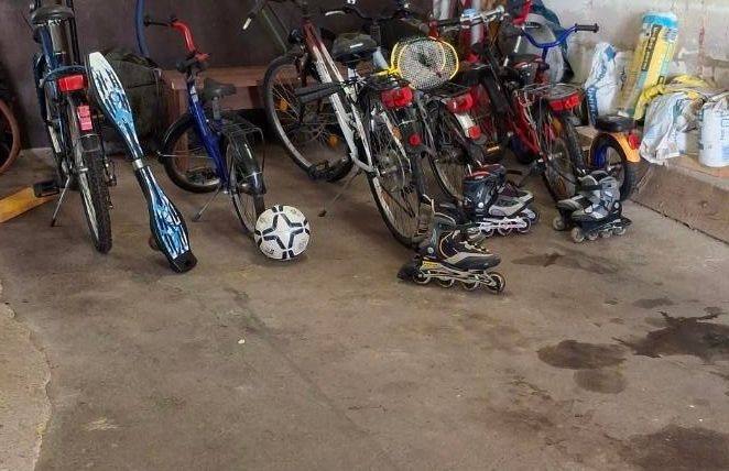 Een rommelige garage met meerdere fietsen en enkele gereedschappen. De vloer is nat en er liggen een paar spullen verspreid.