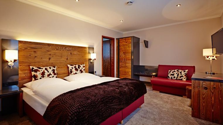 Een modern slaapkamer met een tweepersoonsbed en comfortabele kussens. Er is een rode bank en houten details die de ruimte een warme sfeer geven.