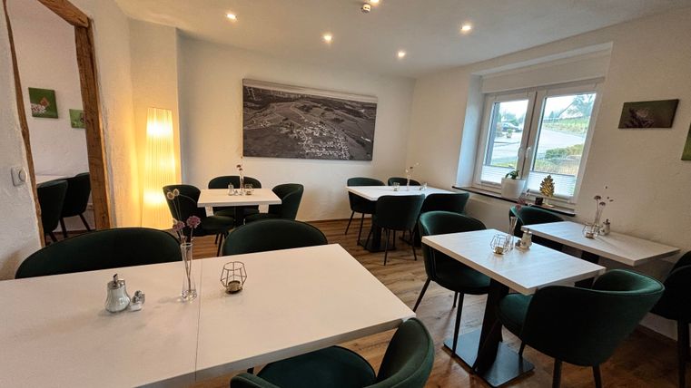 An elegant café with bright tables and green chairs. The space is friendly and modern in design, with large windows and soft lighting.