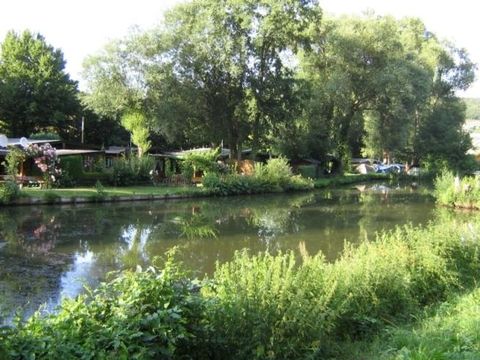 Een rustige rivier, omringd door groene bomen en struiken. Aan de oever zijn enkele tuinhuisjes en boten zichtbaar.