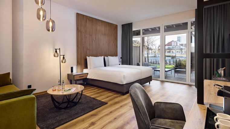 Une chambre moderne avec un grand lit, un canapé vert et de grandes fenêtres. La chambre est lumineuse et décorée avec style, offrant une vue sur l'extérieur.