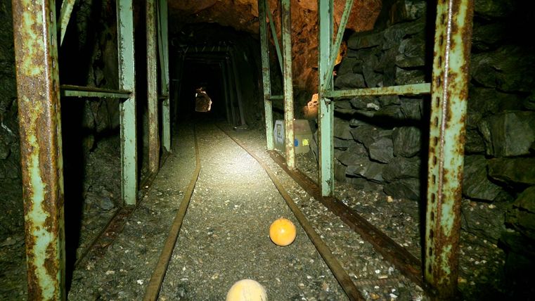 Ein dunkler Tunnel mit rostigen Stützen und Gleisen. Zwei Bälle liegen auf dem Boden.
