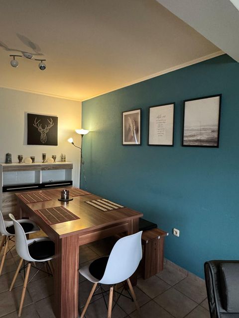 Een moderne eetkamer met een houten tafel en witte stoelen. De muren zijn in een rustgevend blauw geschilderd en er zijn decoratieve afbeeldingen.