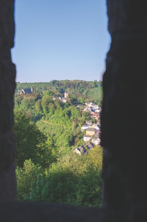 View of a green landscape with a church and houses, framed by dark silhouettes.