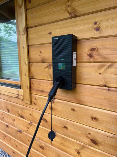 Eine Ladestation für Elektroautos, montiert an einer Holzfassade. Das Kabel hängt bereit zur Nutzung herunter.