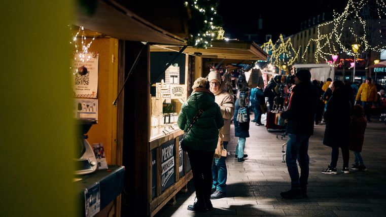 Ein geschäftiger Nachtmarkt mit festlich beleuchteten Ständen. Menschen schauen sich die Waren an und genießen die Atmosphäre.
