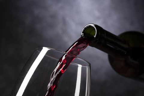 A red wine is being poured from a bottle into a wine glass. The scene is elegantly and darkly set.