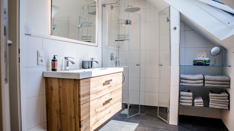 Een moderne badkamer met een douche van glas en een houten wastafel. Handdoeken zijn netjes op een plank gestapeld.