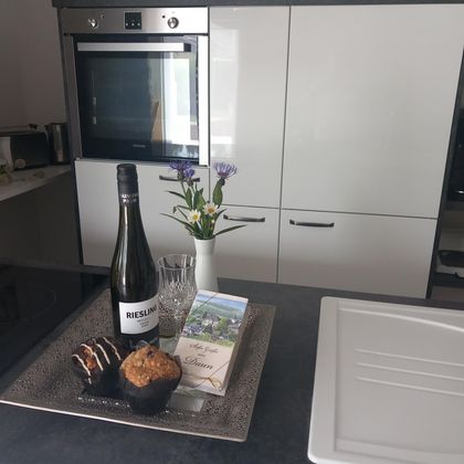 Een moderne keuken met een dienblad dat een fles wijn, glazen, muffins en verse bloemen toont. De ruimte is licht en uitnodigend.