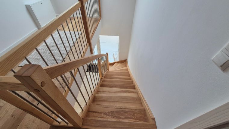 Une belle escalier en bois avec une rampe moderne. La vue descend vers une pièce lumineuse.