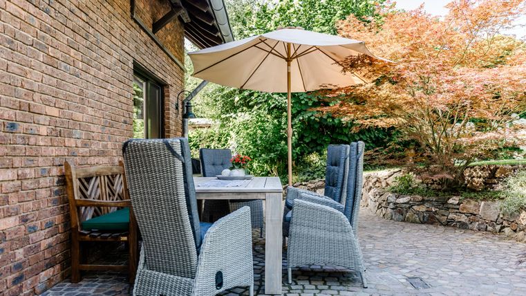 Een gezellige zithoek met een tafel en stoelen onder een parasol. De tuin is groen en verzorgd.