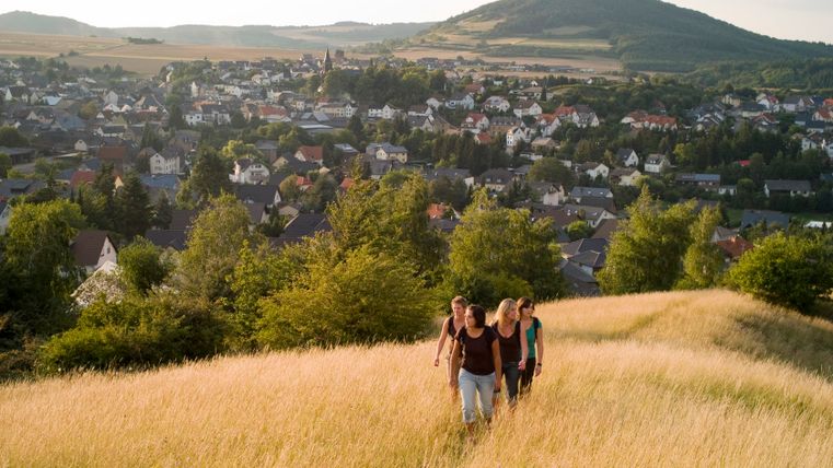 Gruppe von Menschen wandert durch ein Feld mit Blick auf Ettringen im Hintergrund.