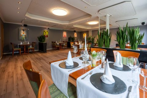 An elegant restaurant with stylishly set tables and modern décor. Green plants and artistic decorations create an inviting atmosphere.