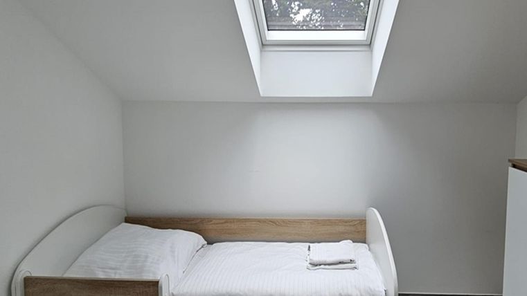 Une chambre simple avec un lit simple et une petite fenêtre. Les murs sont blancs et le sol est gris.