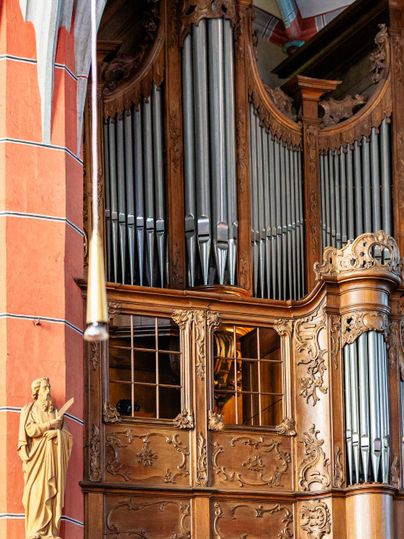 Eine prächtige Kirchenorgel aus Holz mit vielen Pfeifen. Daneben steht eine Statue, die den sakralen Raum ergänzt.